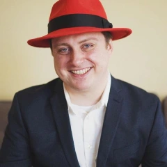photo of Brandon Johnson in a Red Hat fedora with a light tan background